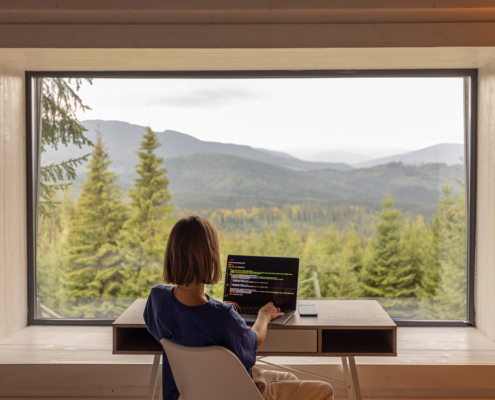 Frau arbeitet am Laptop, während sie am Tisch vor einem Panoramafenster mit herrlichem Blick auf die Berge sitzt.